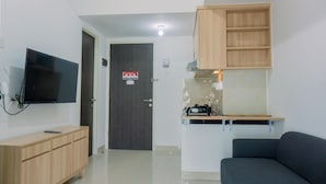 A modern living room with a flat-screen TV, wooden cabinet, and a built-in kitchen area with a microwave and sink. - Minimalist And Comfort 2Br Serpong Garden Apartment (Cisauk)