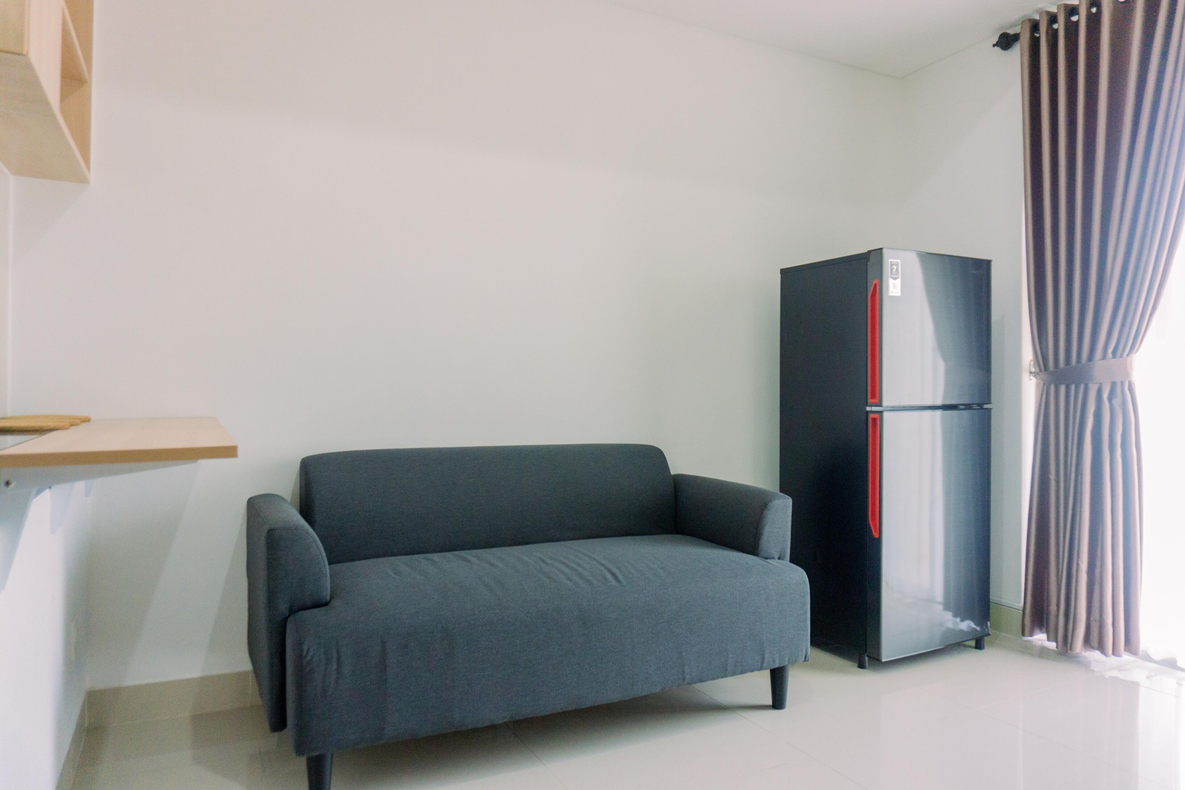 A room with a grey sofa, a black refrigerator, and a wooden shelf.