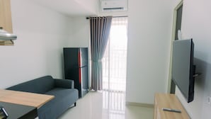 A modern, well-lit room with a sofa, a TV, a wooden table, and a refrigerator. - Minimalist And Comfort 2Br Serpong Garden Apartment (Cisauk)