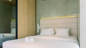 A modern hotel room with a large bed, a wooden headboard, and a large mirror.