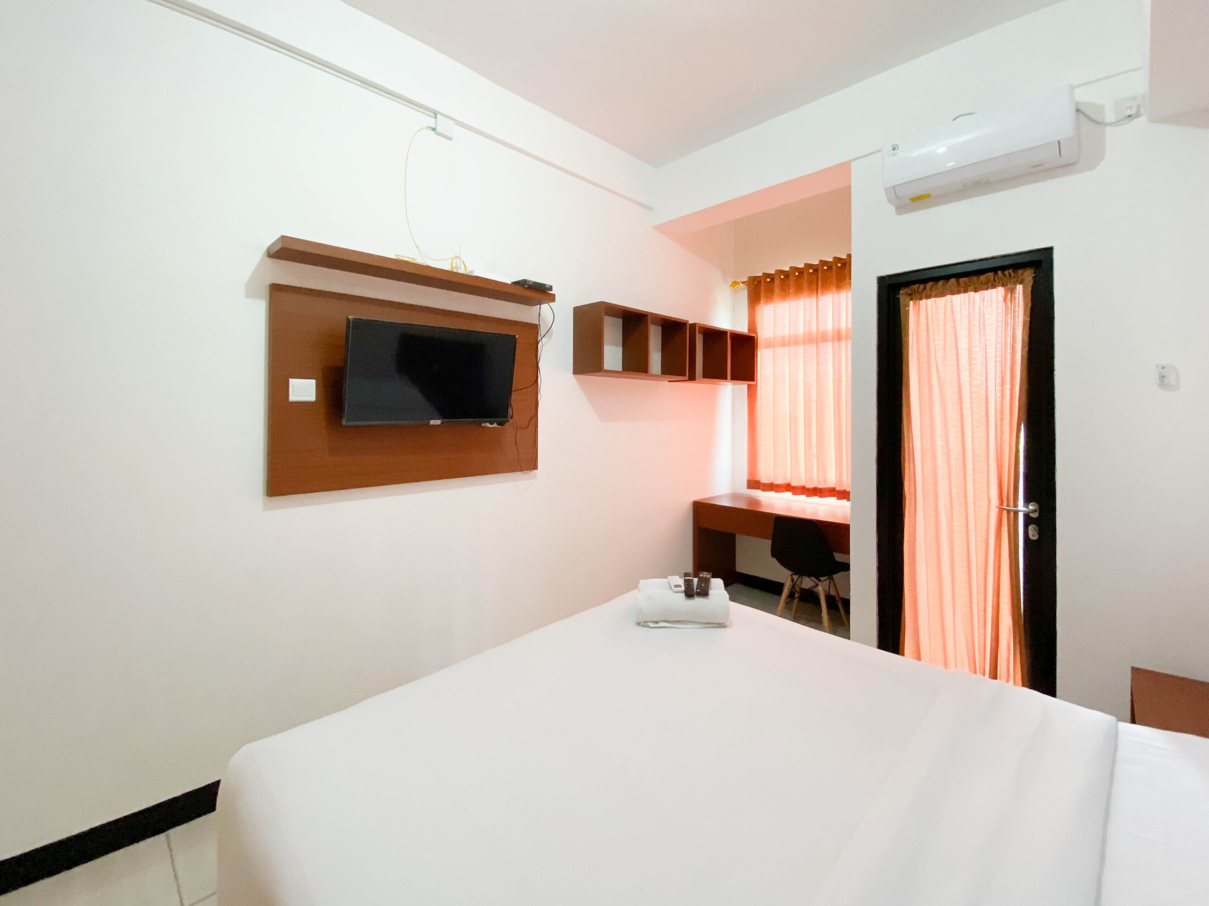 A hotel room with a bed, a TV mounted on the wall, a desk with a chair, and a window with curtains.