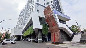 A modern building with a prominent entrance, a parking area with several cars, and a staircase leading to the entrance. - Cozy Stay Studio Cordova Edupartment Semarang Apartment (Semarang)