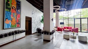 A spacious lobby with a large colorful mural, modern seating, and a view of greenery outside. - Cozy Stay Studio Cordova Edupartment Semarang Apartment (Semarang)
