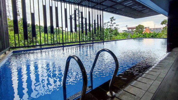 An indoor swimming pool with clear water, metal railings, and a view of greenery and buildings in the background. - Cozy Stay Studio Cordova Edupartment Semarang Apartment (Semarang)