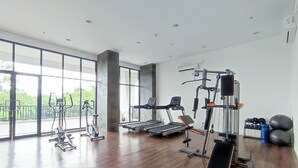 A spacious gym with various exercise equipment, large windows, and a wooden floor. - Cozy Stay Studio Cordova Edupartment Semarang Apartment (Semarang)