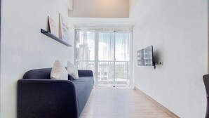 A modern living room with a dark sofa, a mounted TV, and a large window with sheer curtains. - Good Deal 1Br Casa De Parco Apartment Near Aeon Mall (South Tangerang)
