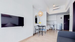 A modern living room with a flat-screen TV, a dining area with a table and chairs, and a kitchen in the background. - Good Deal 1Br Casa De Parco Apartment Near Aeon Mall (South Tangerang)