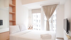 Ein Hotelzimmer mit Bett, Fernseher, Fenster mit Vorhängen und Blick auf Gebäude.