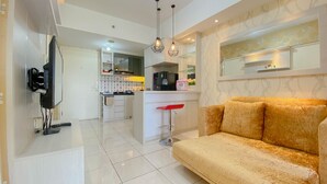 A modern living room with a sofa, a TV mounted on the wall, and a kitchen area in the background.