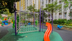 A playground with a slide and climbing structures, surrounded by greenery and residential buildings.