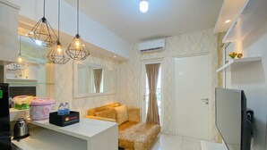 A modern hotel room with a sofa, a TV, a kitchenette, and a glass partition.