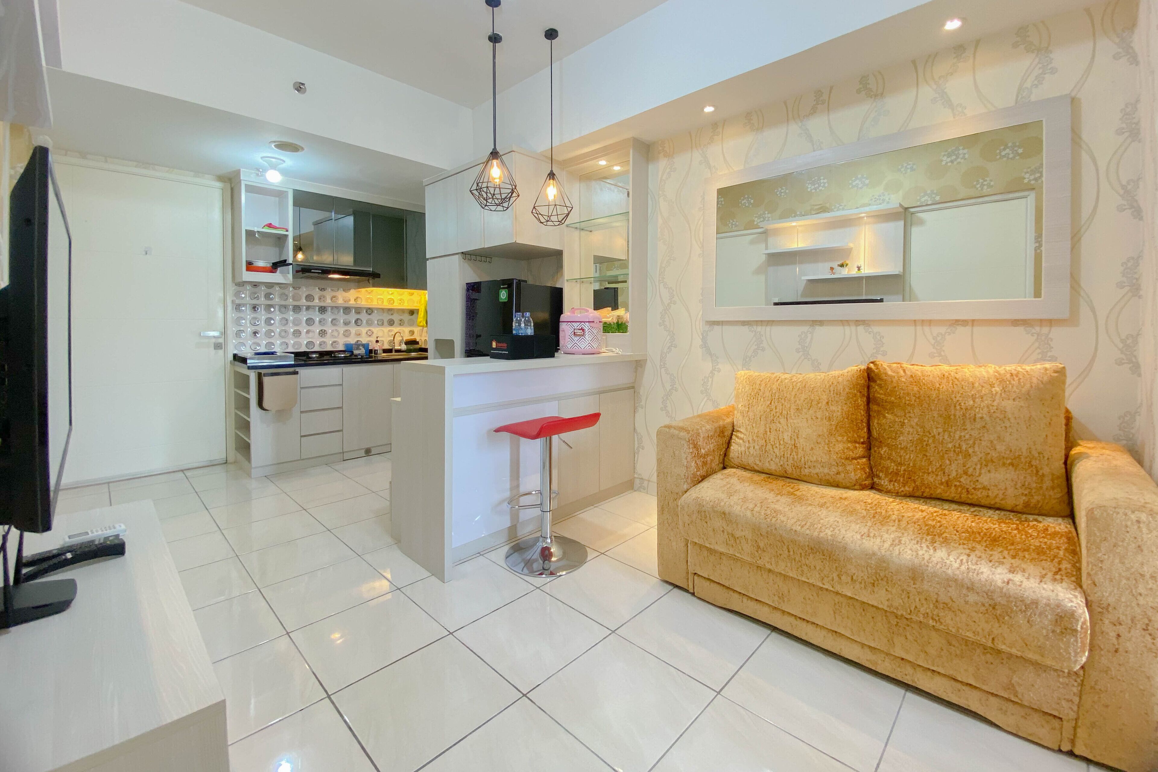 Una sala de estar moderna con un sofá, una zona de cocina con refrigerador, máquina de café y un taburete de bar.