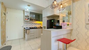 A modern kitchen with white cabinets, a built-in oven, and a refrigerator. There is a red bar stool and a small island with a sink.