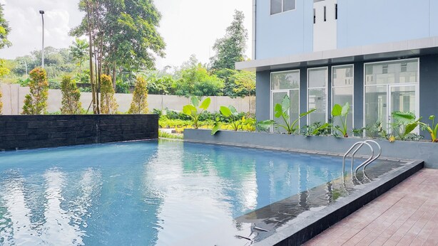 Ein moderner Pool mit Holzterrasse, umgeben von üppiger Vegetation und einem zeitgemäßen Gebäude.