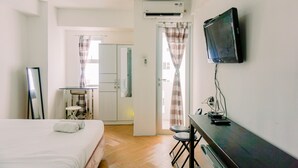Ein Hotelzimmer mit einem Bett, einem Schreibtisch mit Stuhl, einem Fernseher, einer Klimaanlage und Blick auf die Küche und den Essbereich durch eine offene Tür.