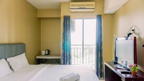 A hotel room with a bed, a desk with a TV, a coffee maker, and a balcony with curtains. - Comfortable And Modern Studio Serpong Greenview Apartment (South Tangerang)