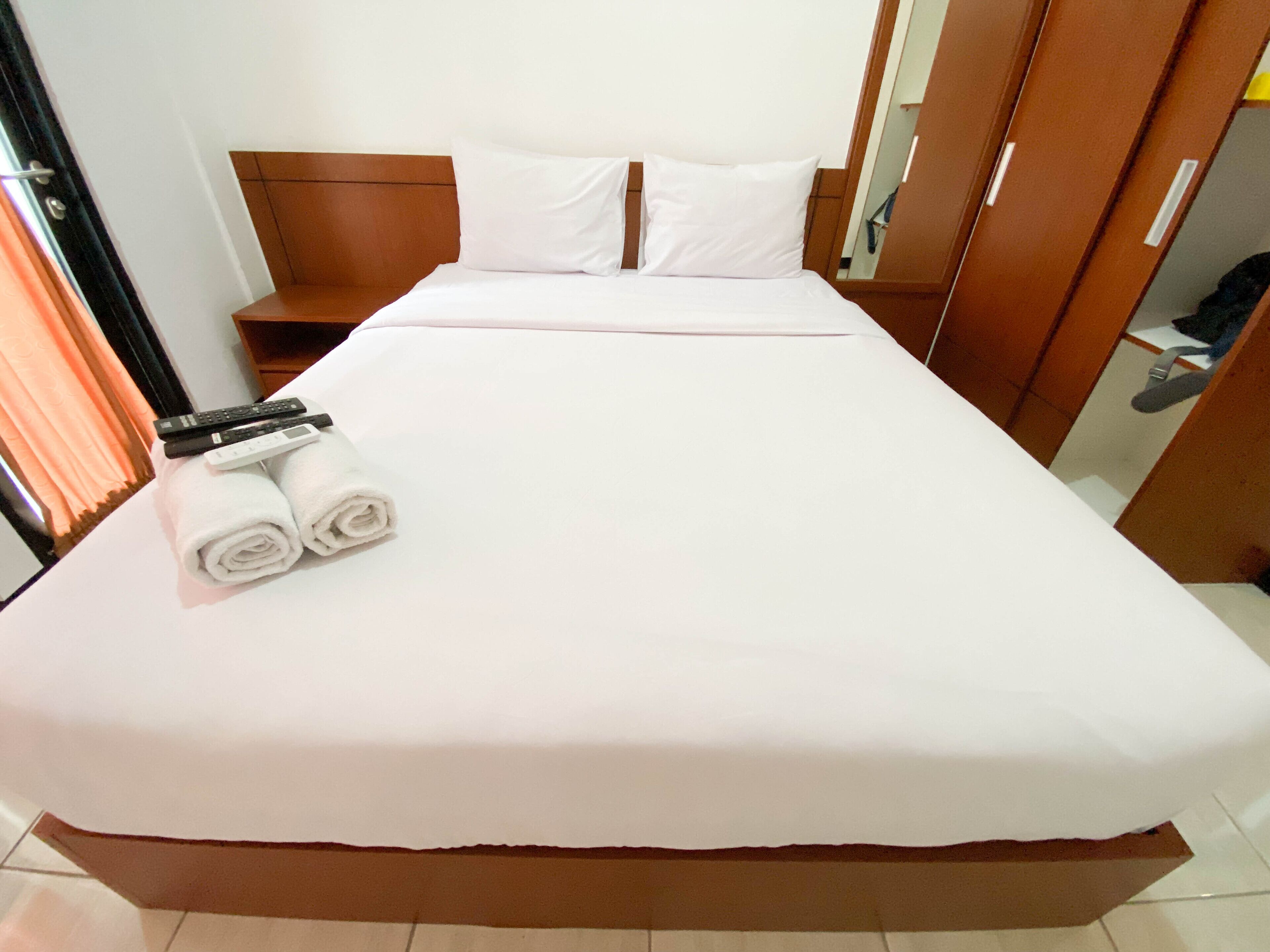 A neatly made bed with white linens, two pillows, and a pair of rolled towels.