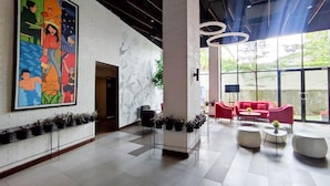 Un hall d’entrée spacieux, agrémenté d’une grande fresque colorée, de mobilier moderne et offrant une vue sur la verdure environnante.