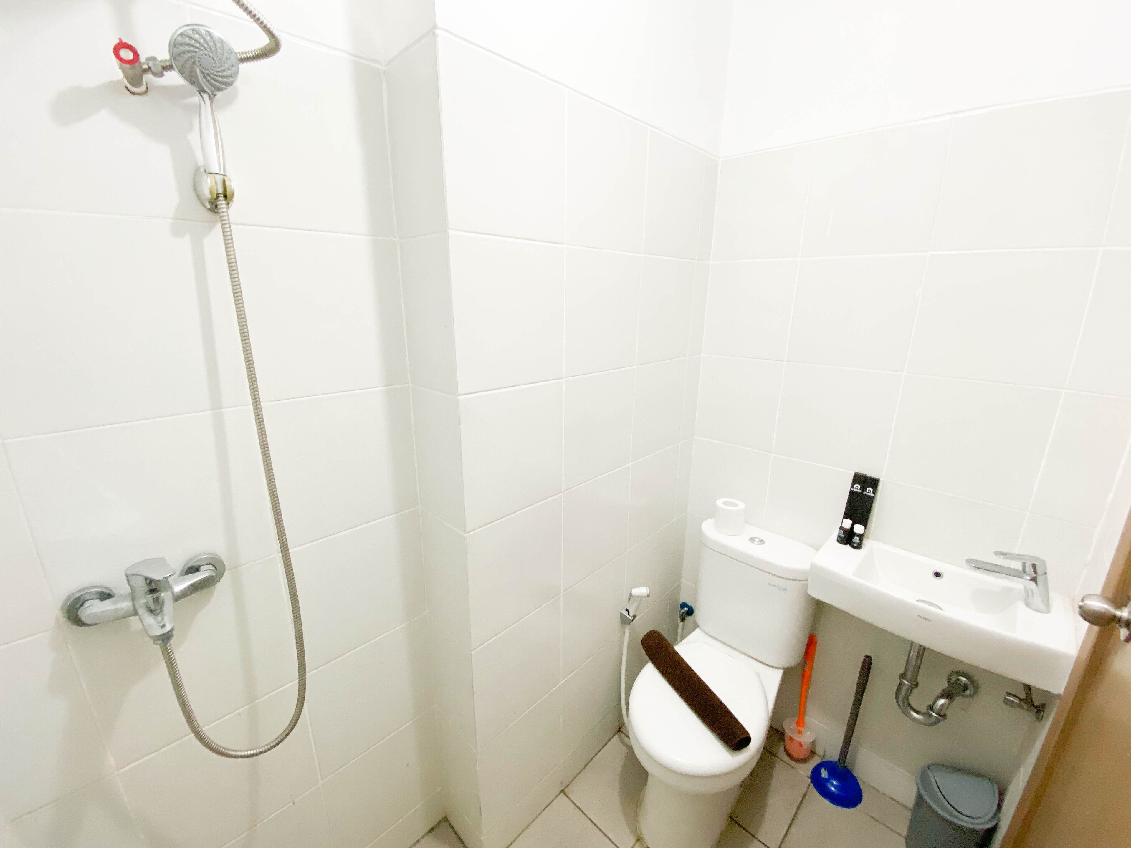 Et badeværelse med brusebad, toilet, håndvask og opbevaring til rengøringsartikler.