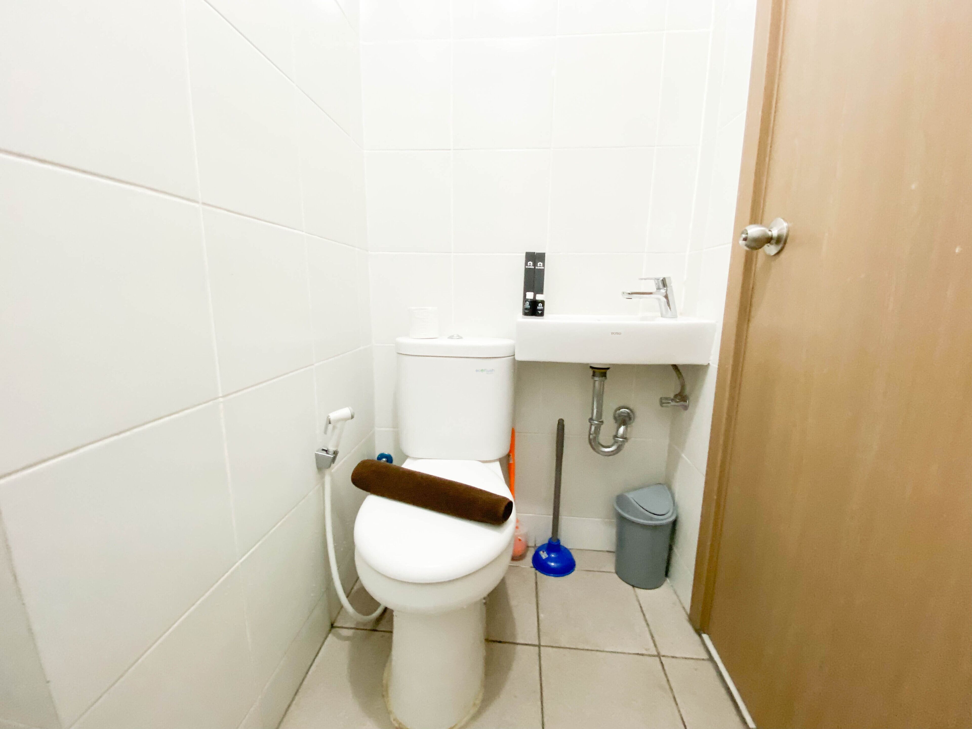A small bathroom with a toilet, a sink, a trash bin, and a door.