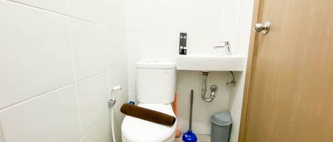 A small bathroom with a toilet, a sink, a trash bin, and a door.