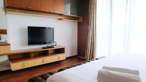 Une chambre d’hôtel avec un lit, un téléviseur posé sur une étagère en bois et une fenêtre avec des rideaux.