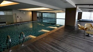 Une piscine dotée d’une terrasse en bois, d’une barrière en verre et d’une chaise placée dans un coin.