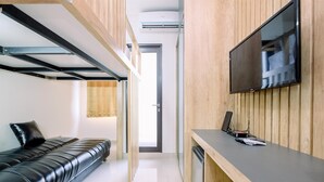 A modern room with a black leather sofa, a wooden desk with a flat-screen TV, and a built-in air conditioning unit. - Minimalist And Good Deal Studio Transpark Cibubur Apartment (Depok)