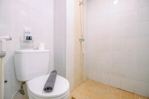A bathroom with a toilet, a shower, and a towel on the seat. - Cozy And Simply Look Studio Room Taman Melati Margonda Apartment (Depok)