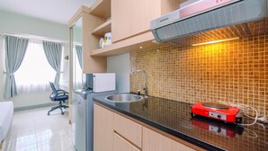 A modern kitchen with a black countertop, stainless steel sink, and a red electric stove. There is a microwave, a cabinet with a white appliance, and a tiled backsplash. - Cozy And Simply Look Studio Room Taman Melati Margonda Apartment (Depok)