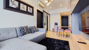 A modern living room with a grey sofa, black and white patterned cushions, a black rug, a coffee machine, and a television. - Scenic And Comfortable 1Br Apartment Branz Bsd City (Pagedangan)