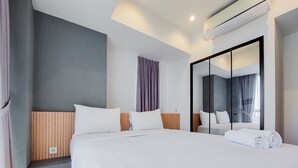 A modern hotel room with a large bed, a wooden headboard, a mirror, and a neatly made bed with rolled towels. - Scenic And Comfortable 1Br Apartment Branz Bsd City (Pagedangan)