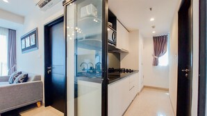 A modern kitchen with a glass door, a grey sofa, and a dining area with a table and chairs. - Scenic And Comfortable 1Br Apartment Branz Bsd City (Pagedangan)