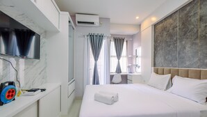 Una habitación de hotel con una cama grande, un televisor montado en la pared, un escritorio con una silla y un baño visible a través de una puerta abierta.