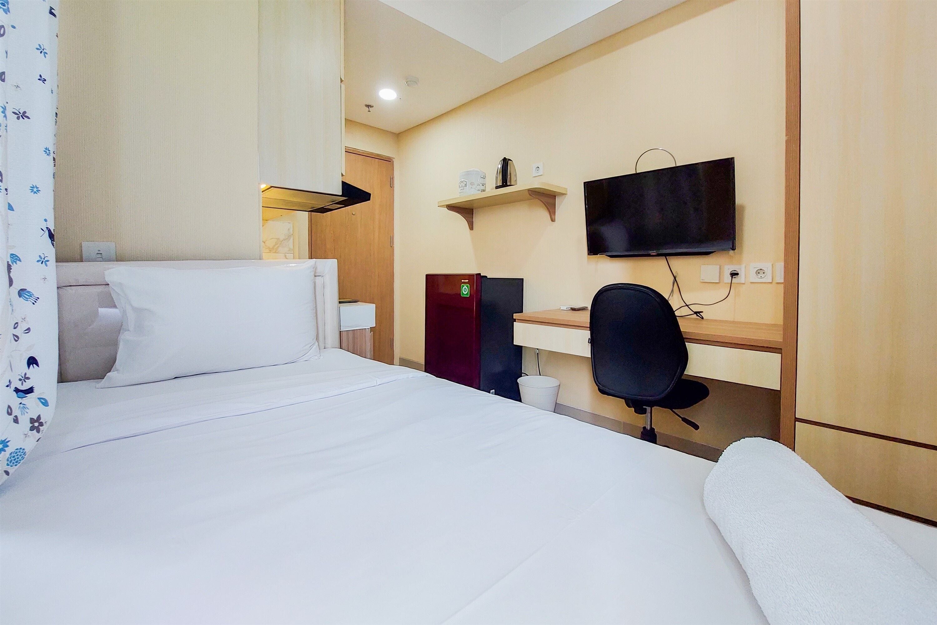 Una habitación de hotel con cama, escritorio, silla, televisor y refrigerador.