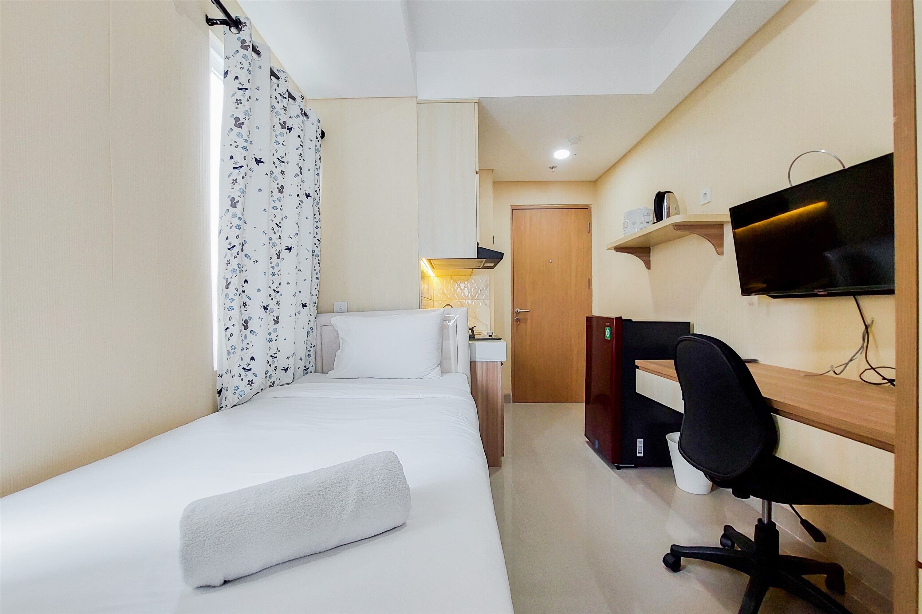 A hotel room with a bed, a desk, a chair, a television, and a door.