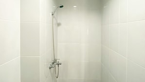 Um chuveiro com um chuveiro manual e uma torneira fixada na parede, em um banheiro revestido com azulejos.