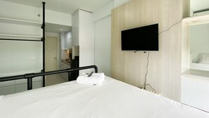 Quarto de hotel com uma cama, televisão presa à parede e banheiro visível por uma porta aberta.