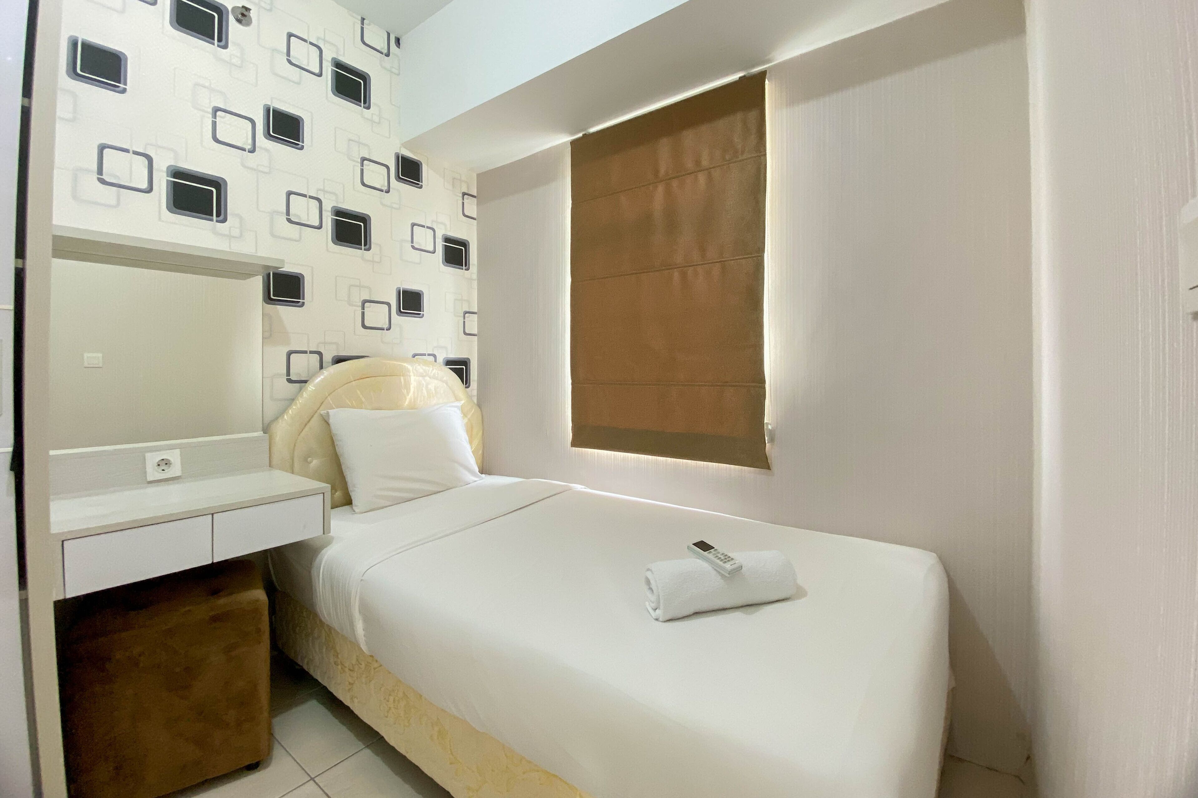 A neatly arranged bedroom with a bed, a bedside table, a mirror, and a window with a brown blind.