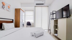 A hotel room with a bed, a TV, a wardrobe, and a desk with a chair. - Homey And Warm Studio Room Serpong Garden Apartment (Cisauk)