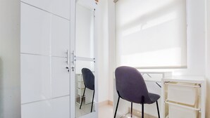 A room with a white wardrobe, a chair, and a white desk with shelves. - Homey And Warm Studio Room Serpong Garden Apartment (Cisauk)