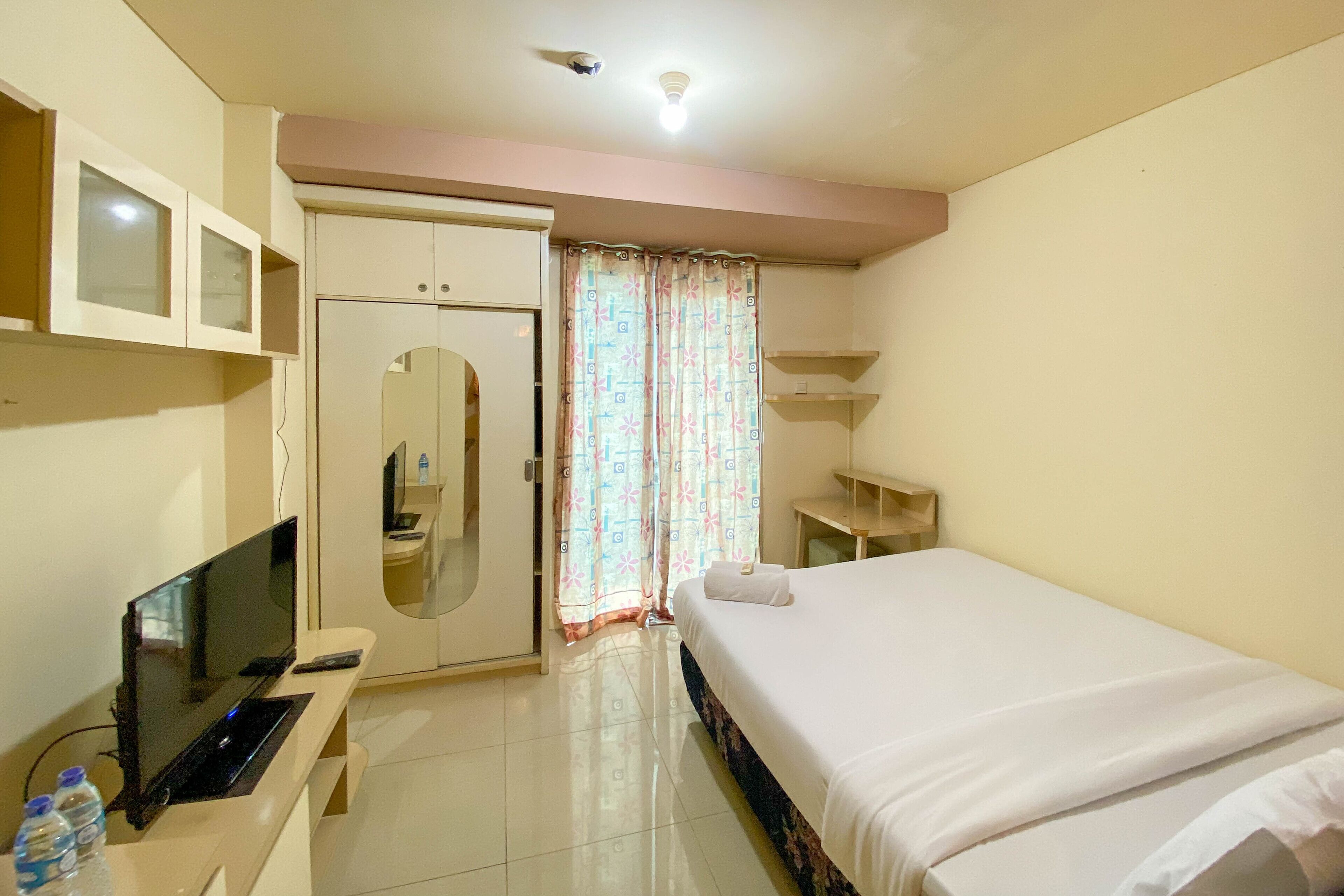 Une chambre d’hôtel équipée d’un lit, d’une télévision, d’un miroir, d’une armoire et d’une fenêtre avec des rideaux.