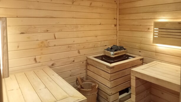 A sauna with wooden walls and benches, a heated stone basin, and a small trash bin.