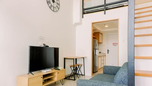 A modern living room with a flat-screen TV, a wooden TV stand, a small table, and a blue sofa. - Modern And Cozy Studio Loft Apartment At Kingland Avenue (South Tangerang)
