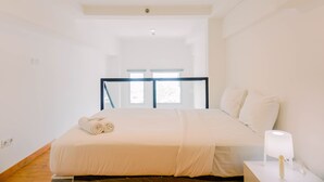 A modern bedroom with a large bed, a nightstand with a lamp, and a view of the outdoors through a window. - Modern And Cozy Studio Loft Apartment At Kingland Avenue (South Tangerang)