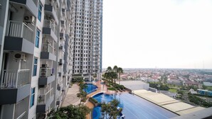 A high-rise residential building with balconies, a swimming pool, and a view of a residential area. - Cozy Living 2Br At Anderson Supermall Mansion Apartment (Surabaya)