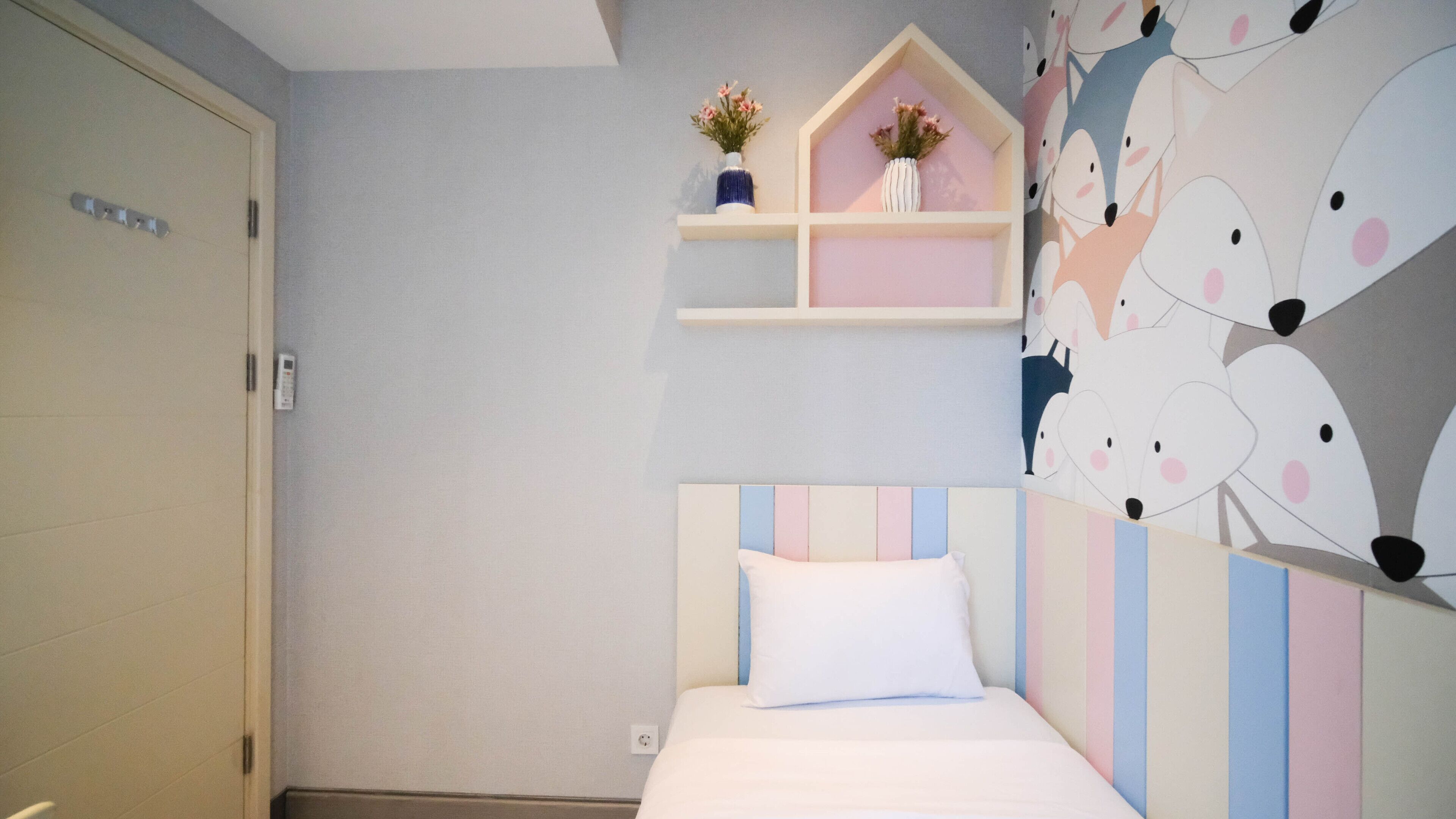 Een slaapkamer met een bed, een kledingkast, een plank met bloemen en een muur met een patroon van een cartooneske dierenprint.