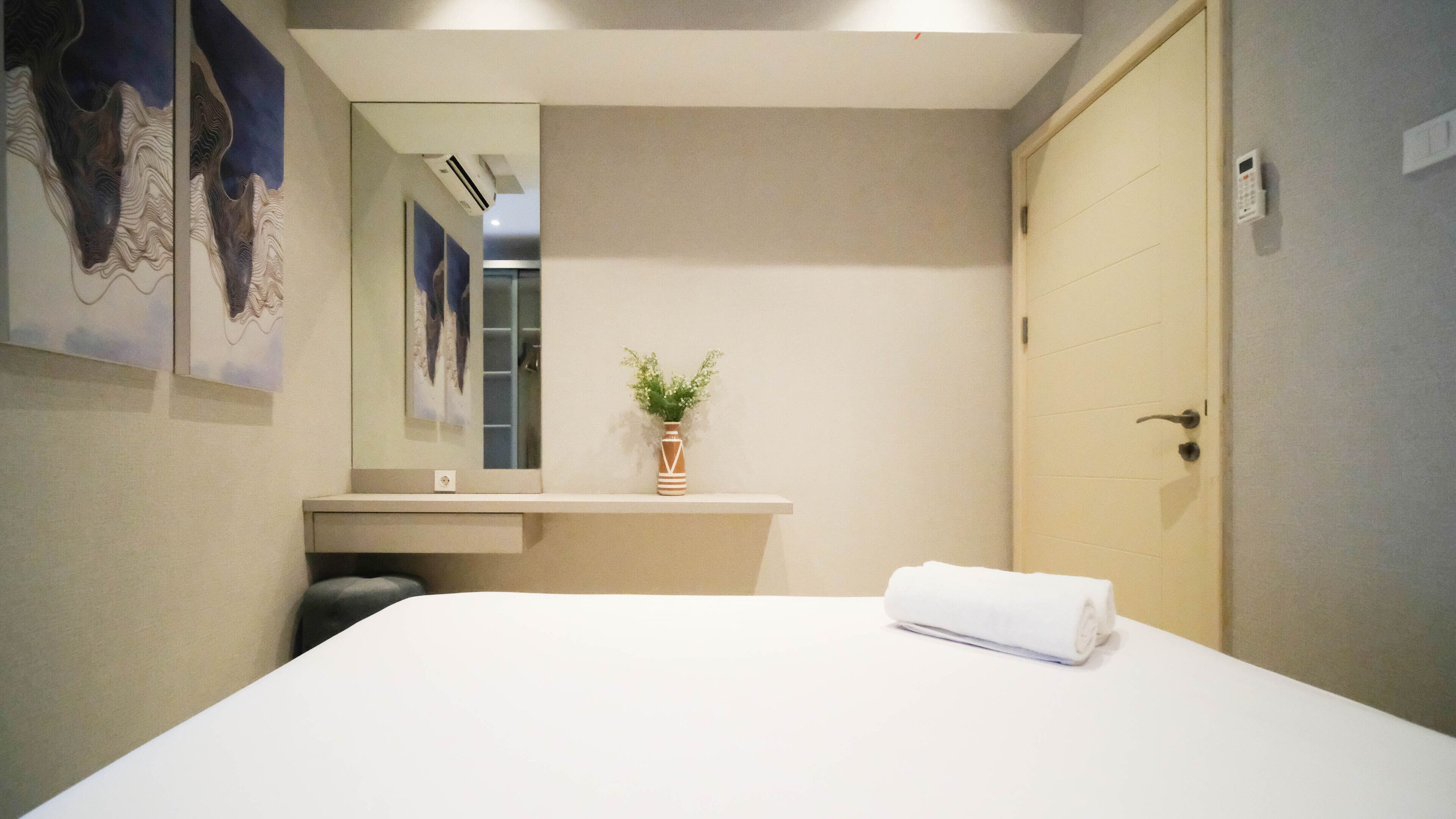 Habitació d'hotel moderna amb un llit gran, una petita taula de nit amb un ram i un mirall, i una porta.