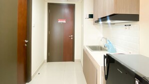 A compact kitchen with a refrigerator, sink, and wooden cabinets. - Cozy Studio Room At Pollux Chadstone Apartment (Cikarang)