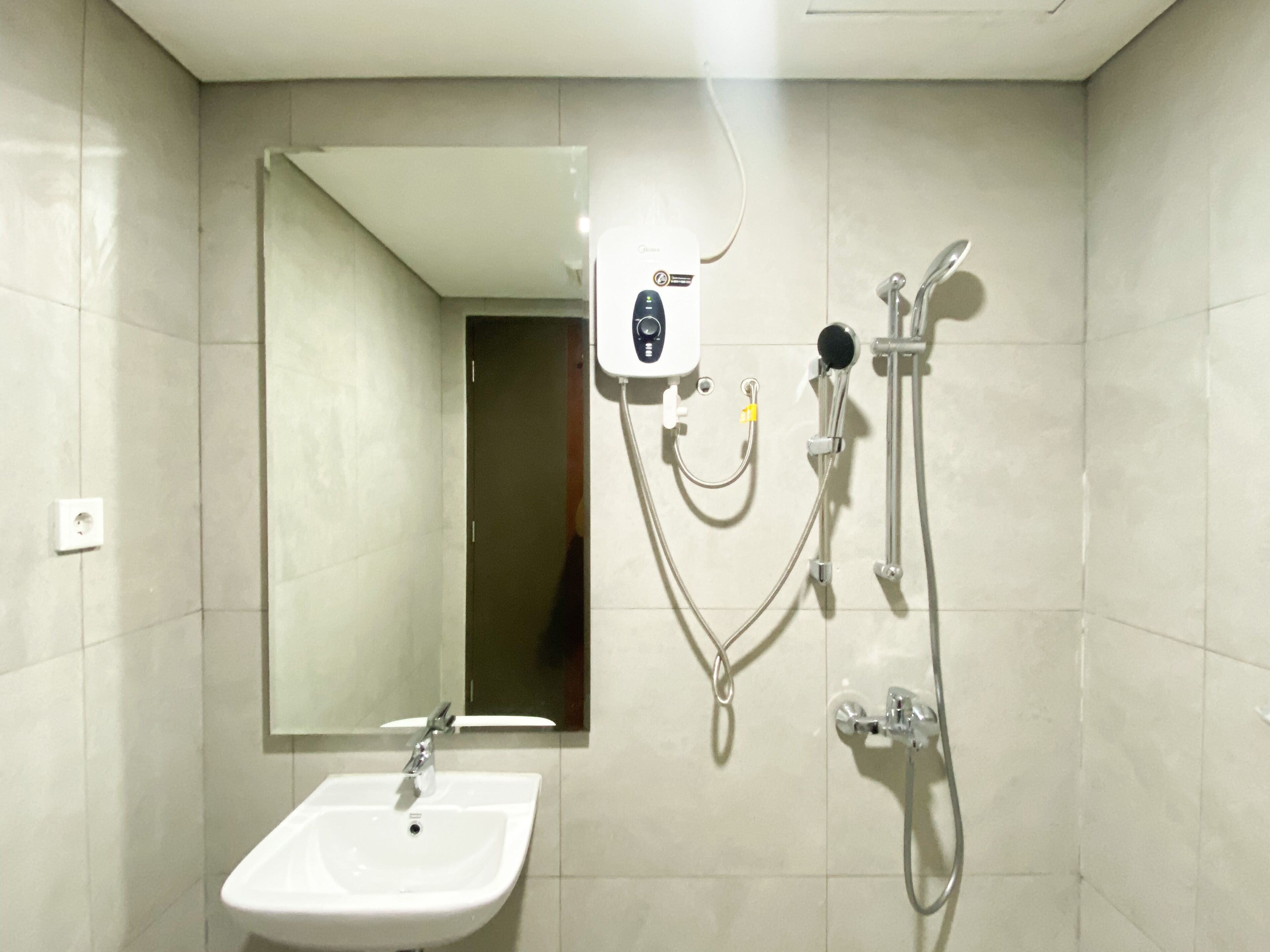 Casa de banho com lavatório branco, espelho e cabine de duche com chuveiro manual e um acessório de duche de mão.